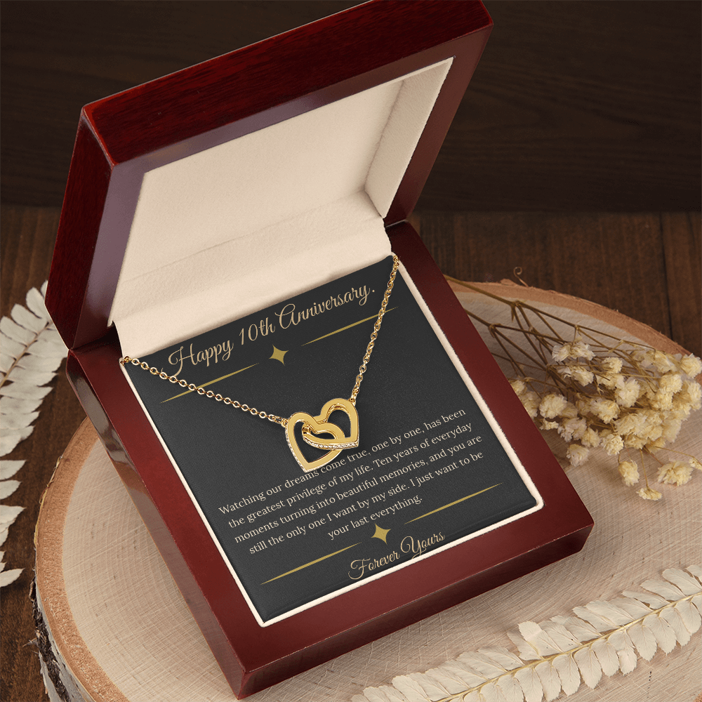 10th Anniversary gift for wife featuring a silver and rose gold interlocking hearts necklace inside a luxury mahogany LED box. The necklace rests on a dark premium message card with gold dividers and a romantic quote about dreams coming true.