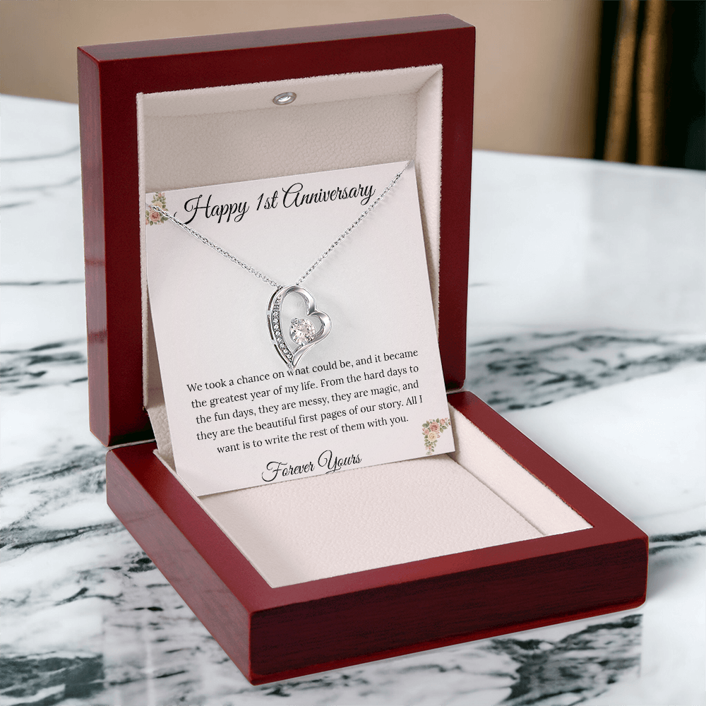 1st Anniversary gift for wife featuring a Forever Love heart necklace inside a luxury mahogany LED box. The pendant rests on a soft blush message card with blue floral corners and a romantic "messy and magic" quote