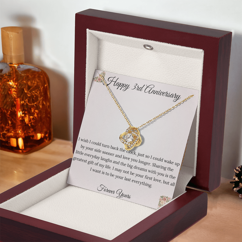 3rd Anniversary gift for wife featuring a brilliant Love Knot necklace inside a luxury mahogany LED box. The pendant rests on a soft blush message card with warm pink floral corners and a romantic "last everything" quote
