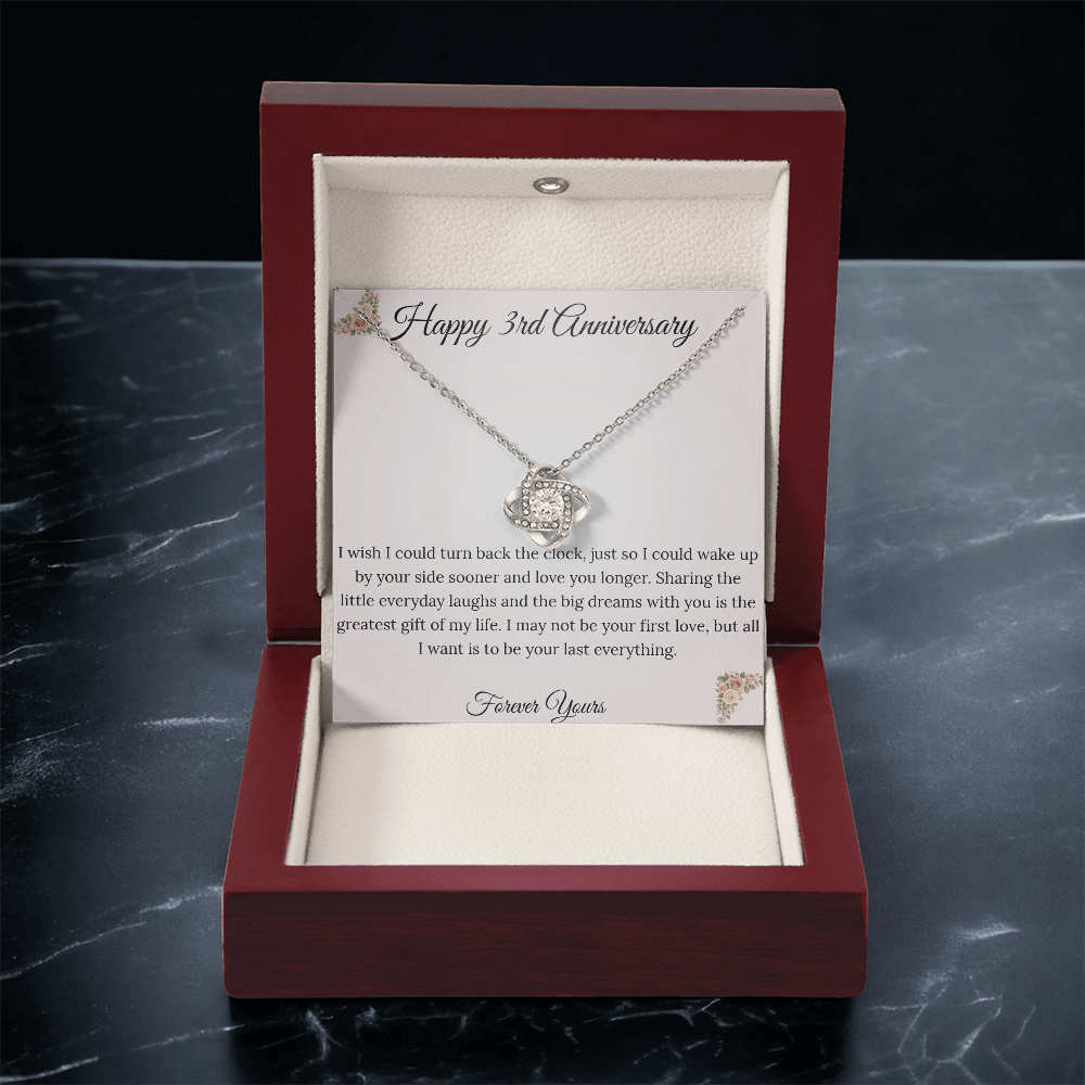 3rd Anniversary gift for wife featuring a brilliant Love Knot necklace inside a luxury mahogany LED box. The pendant rests on a soft blush message card with warm pink floral corners and a romantic "last everything" quote