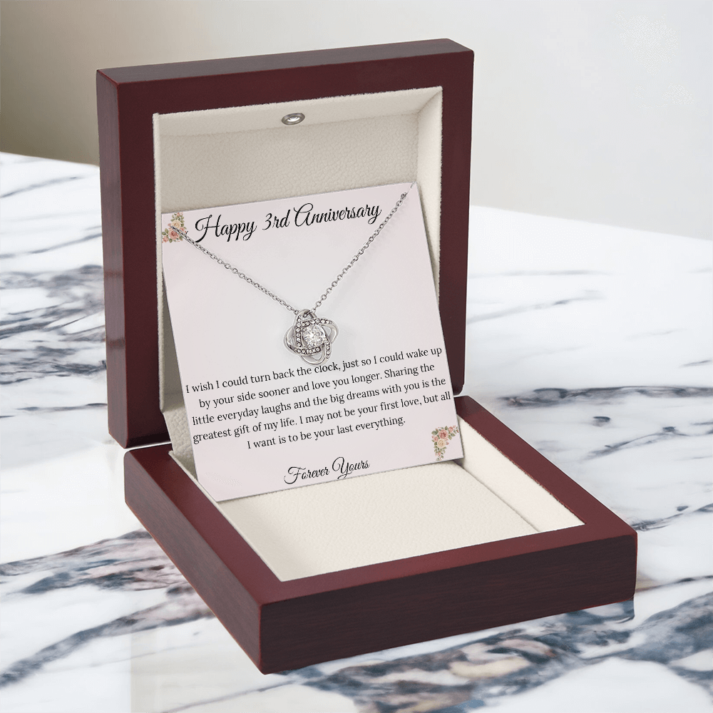3rd Anniversary gift for wife featuring a brilliant Love Knot necklace inside a luxury mahogany LED box. The pendant rests on a soft blush message card with warm pink floral corners and a romantic "last everything" quote