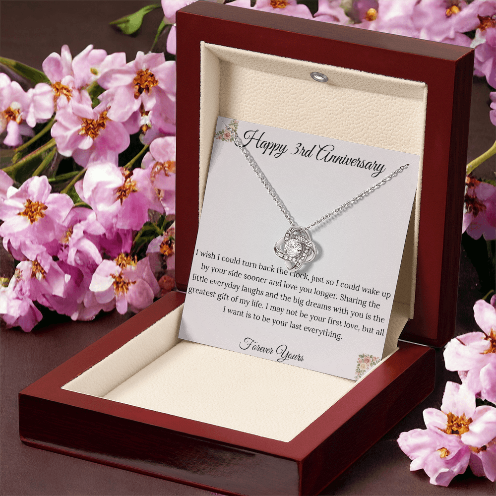 3rd Anniversary gift for wife featuring a brilliant Love Knot necklace inside a luxury mahogany LED box. The pendant rests on a soft blush message card with warm pink floral corners and a romantic "last everything" quote