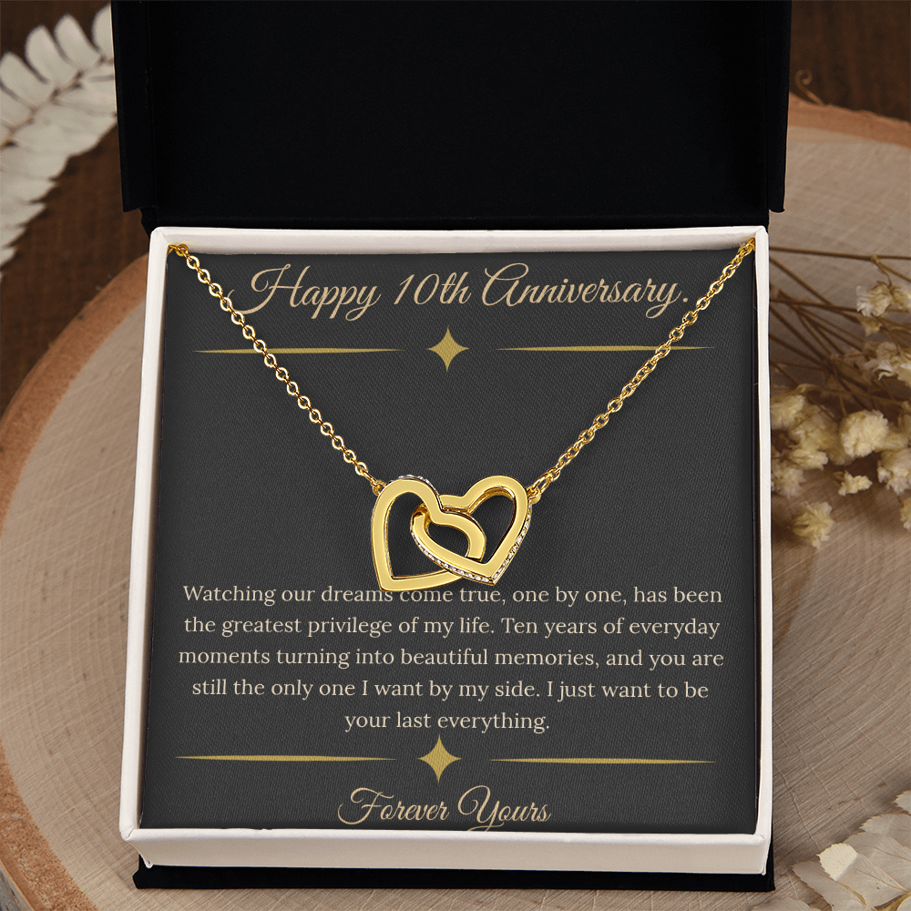 10th Anniversary gift for wife featuring a silver and rose gold interlocking hearts necklace inside a luxury mahogany LED box. The necklace rests on a dark premium message card with gold dividers and a romantic quote about dreams coming true.