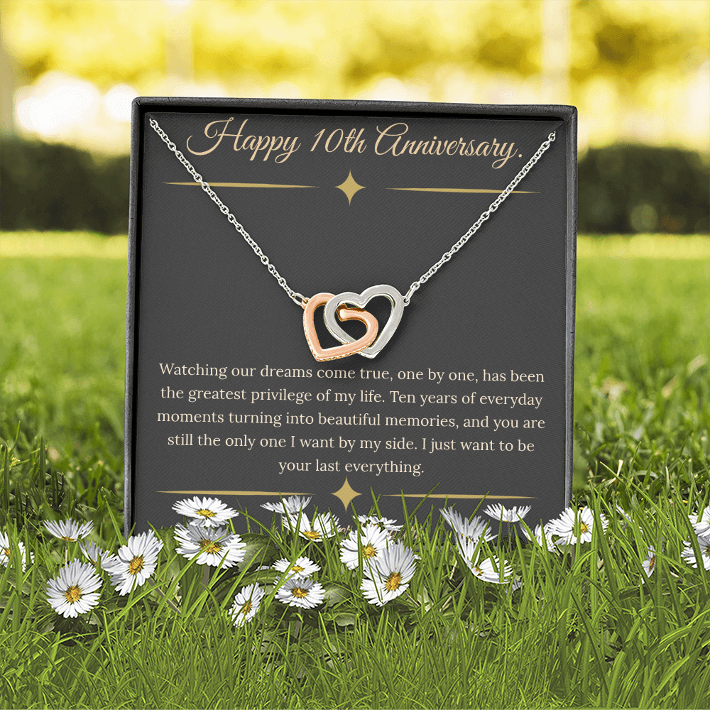 10th Anniversary gift for wife featuring a silver and rose gold interlocking hearts necklace inside a luxury mahogany LED box. The necklace rests on a dark premium message card with gold dividers and a romantic quote about dreams coming true.
