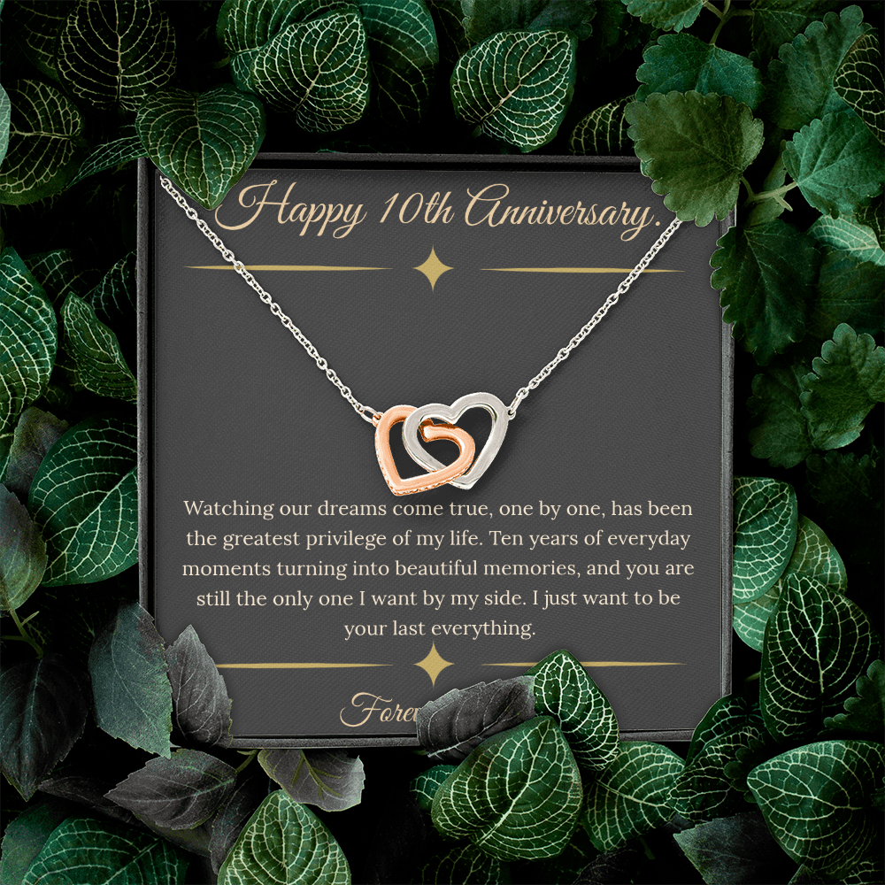 10th Anniversary gift for wife featuring a silver and rose gold interlocking hearts necklace inside a luxury mahogany LED box. The necklace rests on a dark premium message card with gold dividers and a romantic quote about dreams coming true.