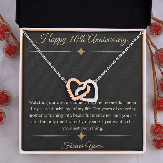 10th Anniversary gift for wife featuring a silver and rose gold interlocking hearts necklace inside a luxury mahogany LED box. The necklace rests on a dark premium message card with gold dividers and a romantic quote about dreams coming true.