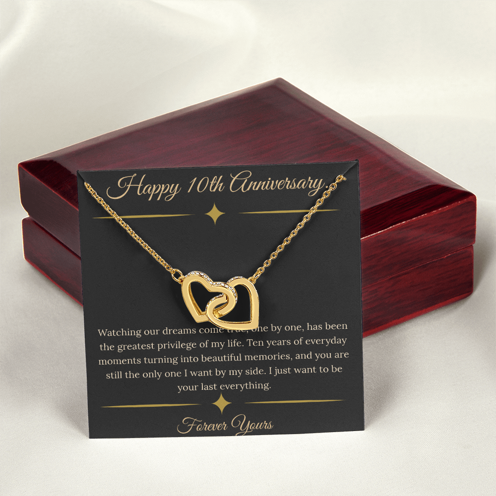 10th Anniversary gift for wife featuring a silver and rose gold interlocking hearts necklace inside a luxury mahogany LED box. The necklace rests on a dark premium message card with gold dividers and a romantic quote about dreams coming true.