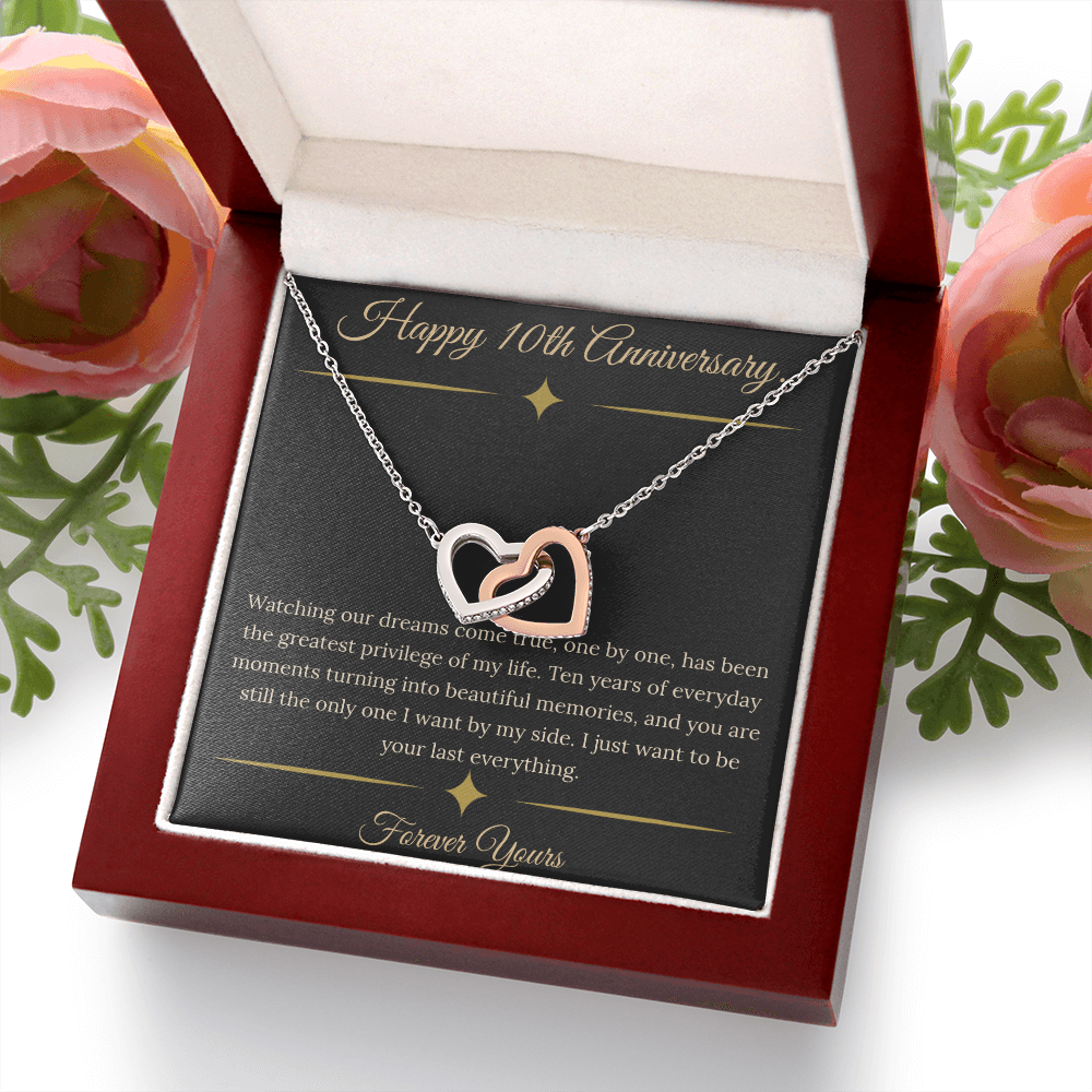 10th Anniversary gift for wife featuring a silver and rose gold interlocking hearts necklace inside a luxury mahogany LED box. The necklace rests on a dark premium message card with gold dividers and a romantic quote about dreams coming true.