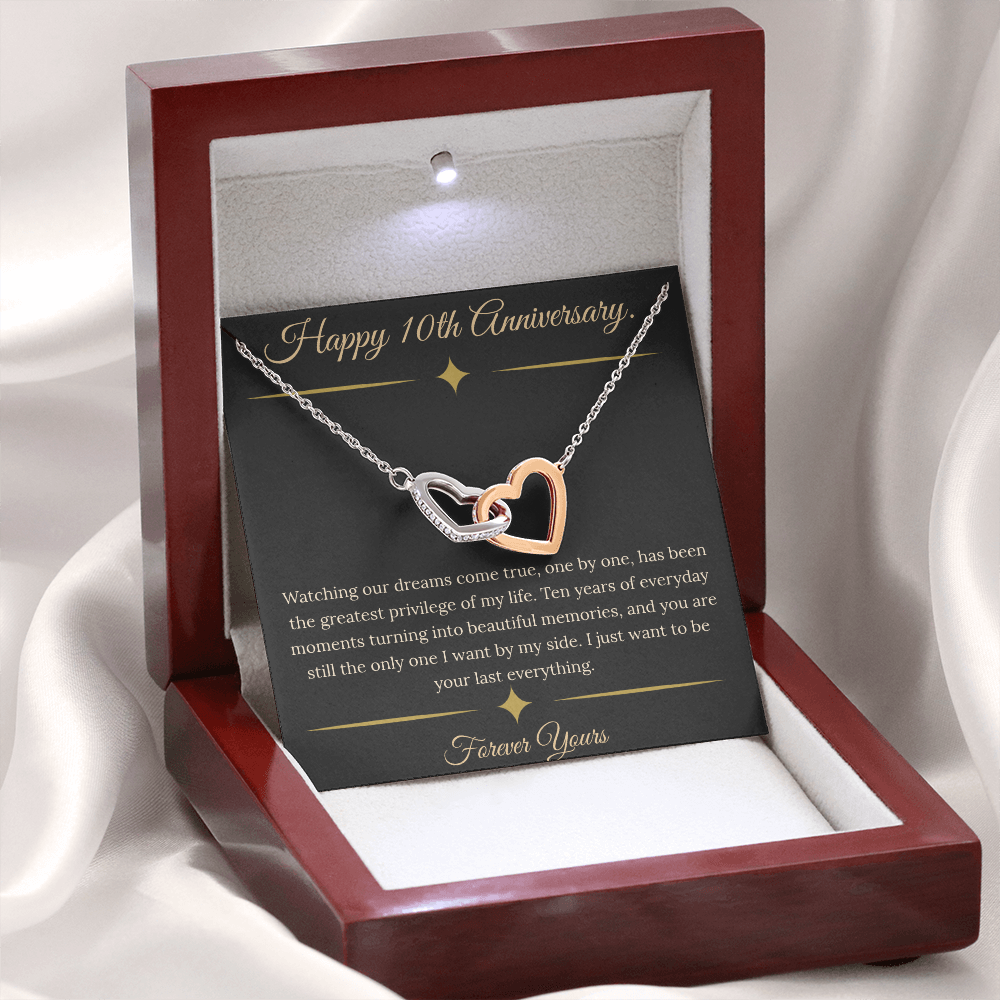 10th Anniversary gift for wife featuring a silver and rose gold interlocking hearts necklace inside a luxury mahogany LED box. The necklace rests on a dark premium message card with gold dividers and a romantic quote about dreams coming true.