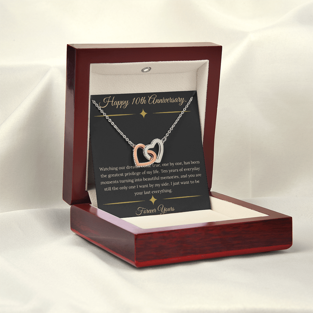 10th Anniversary gift for wife featuring a silver and rose gold interlocking hearts necklace inside a luxury mahogany LED box. The necklace rests on a dark premium message card with gold dividers and a romantic quote about dreams coming true.