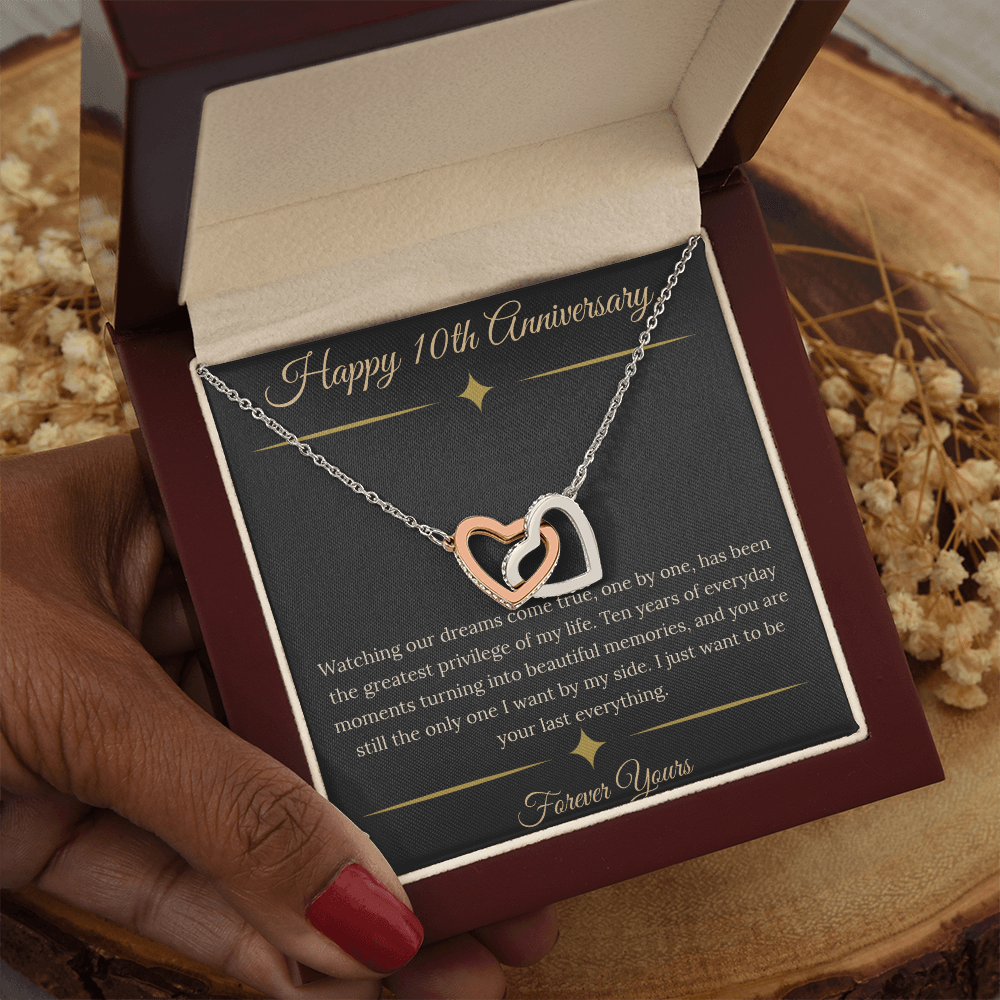 10th Anniversary gift for wife featuring a silver and rose gold interlocking hearts necklace inside a luxury mahogany LED box. The necklace rests on a dark premium message card with gold dividers and a romantic quote about dreams coming true.