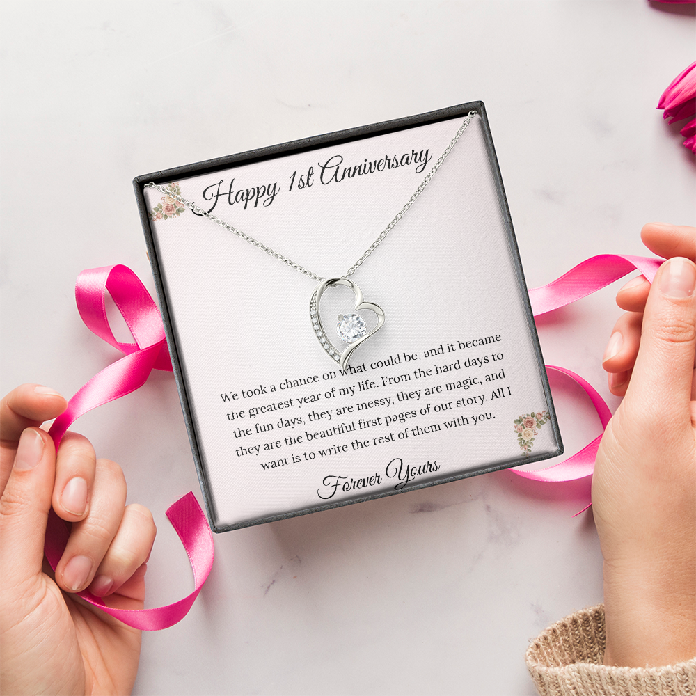 1st Anniversary gift for wife featuring a Forever Love heart necklace inside a luxury mahogany LED box. The pendant rests on a soft blush message card with blue floral corners and a romantic "messy and magic" quote